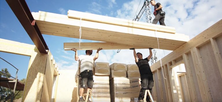 Drei Mitarbeiter sind mitten in der Montage von mehreren Holzbalken.