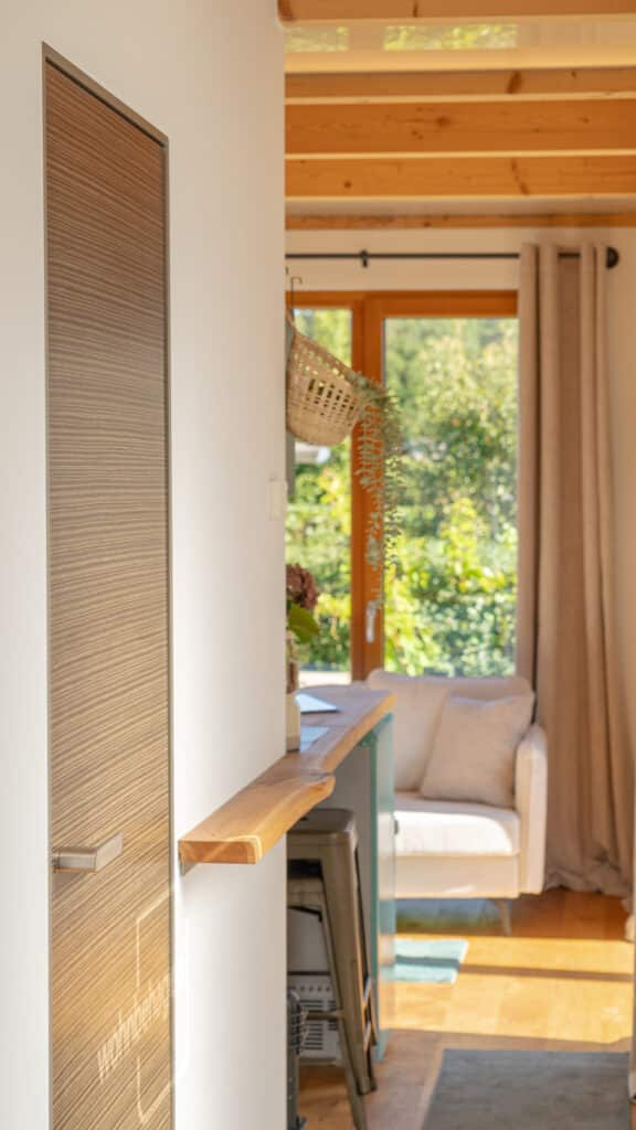 Eine lichtdurchflutete, gemütliche Wohnstube spiegelt durch natürliche Materialien und modernes Design die Harmonie eines nachhaltigen Holzhauses wider. Einladendes Sofa, sanfte Vorhänge und Sicht ins Grüne schaffen Wärme und Behaglichkeit.